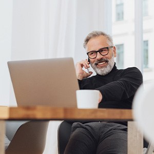 Man with glasses smiling while working on laptop