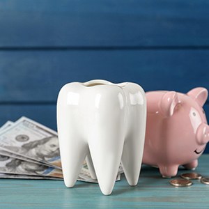 A large ceramic tooth model next to a piggy bank and some dollar bills