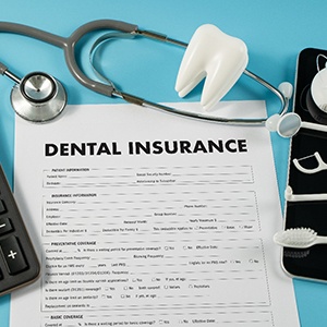 A dental insurance form next to a calculator and some dental tools