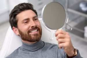Man smiling in mirror after cosmetic dental treatment