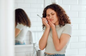 Woman holding toothbrush and holding other hand to face in pain.